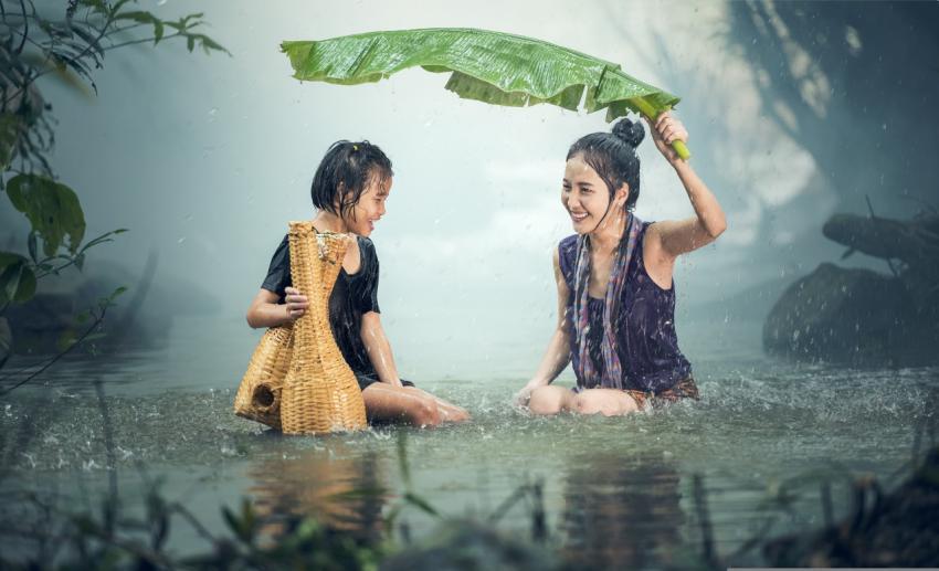 A woman with a child hiding from the rain under a large leaf